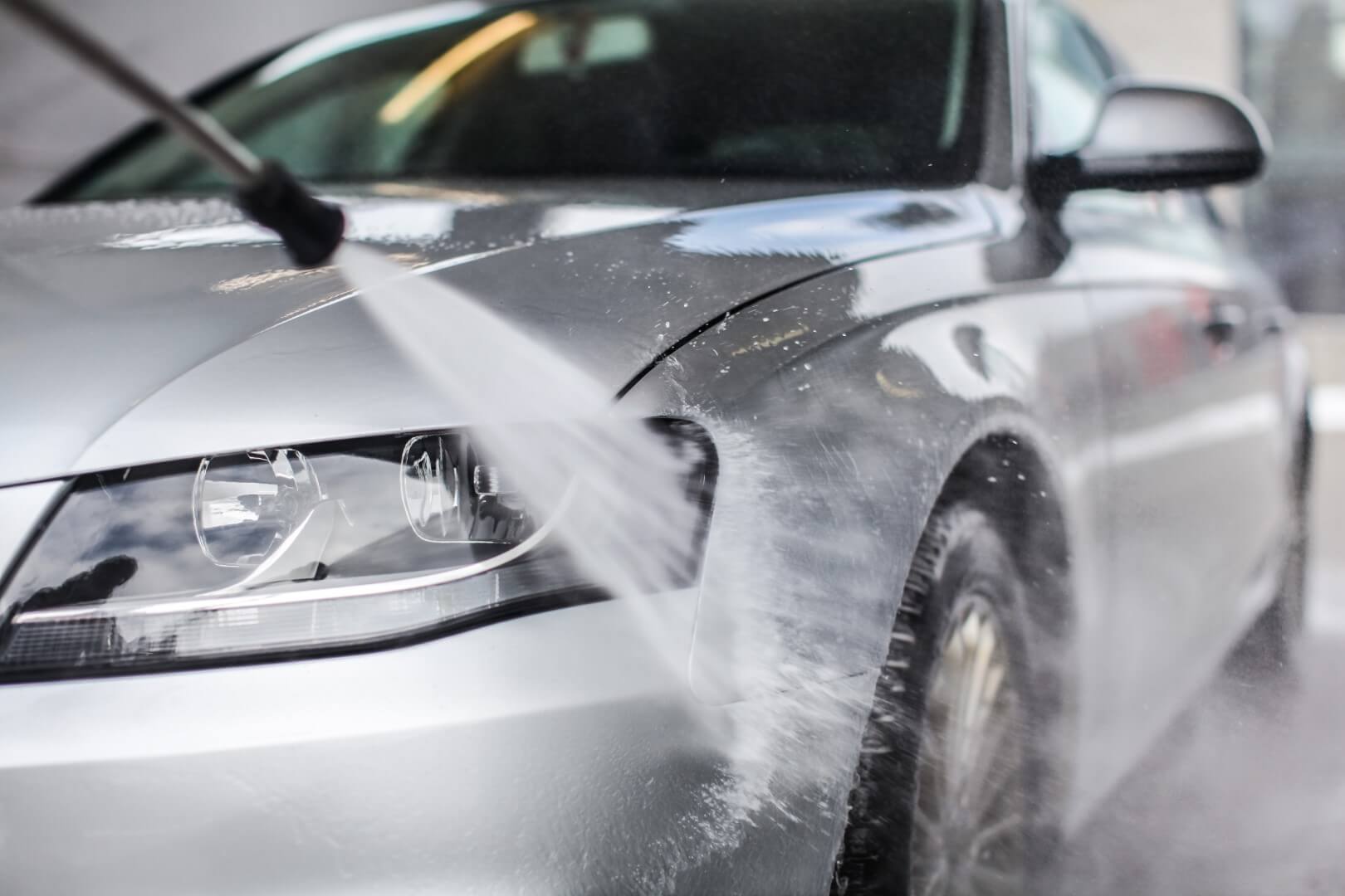 Image depicts a car detailing expert washing the exterior of a car.